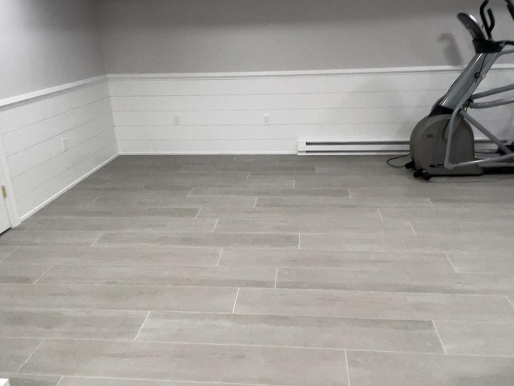 Tile floor installation in a modern home gym with clean gray tiles and seamless alignment.
