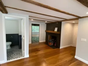 Interior renovation project showing hardwood floors, exposed beams, and updated bathroom entrance.