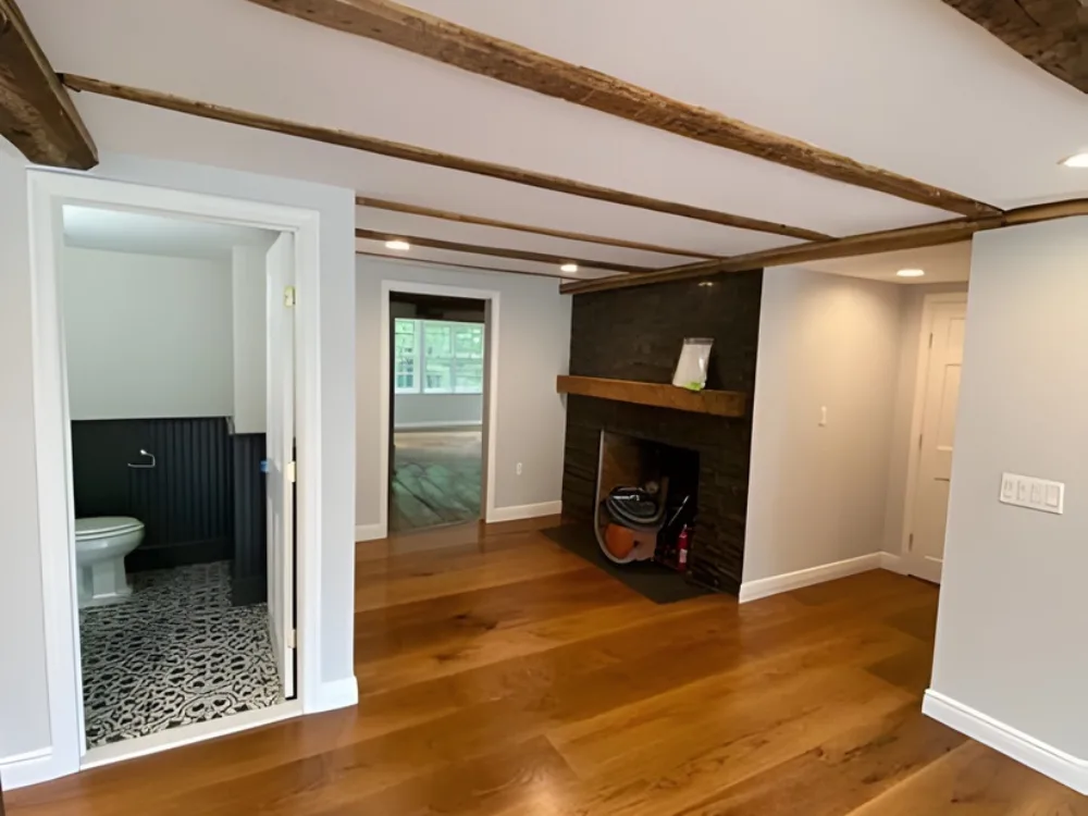 Interior renovation project showing hardwood floors, exposed beams, and updated bathroom entrance.